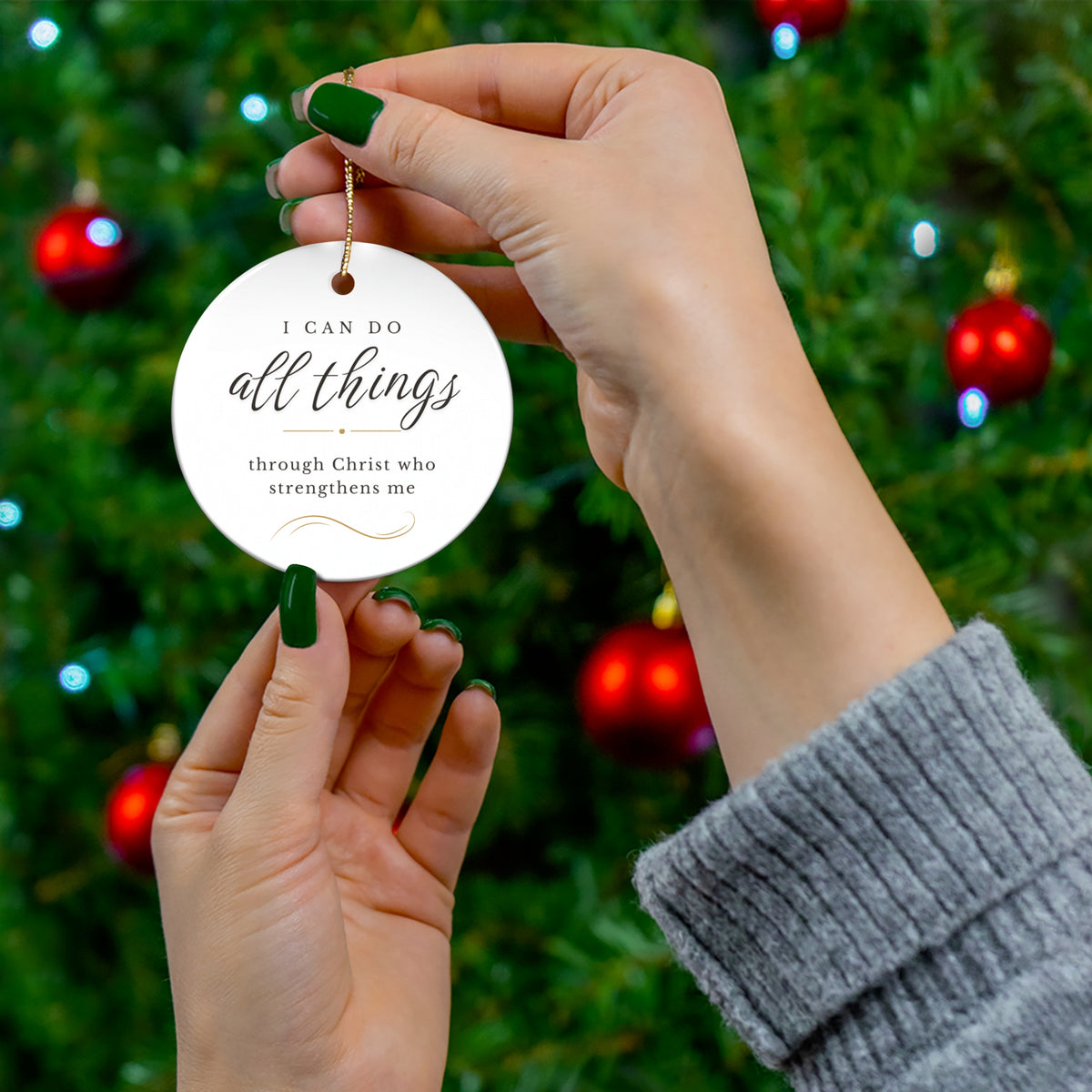 Person holding a white ornament with I can do all things through Christ who strengthens me against a Christmas tree background